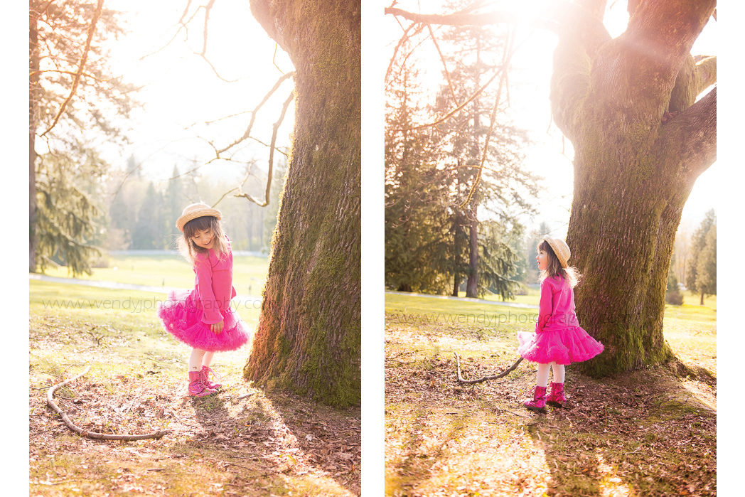 Young girl on a sunny day stands beside a large tree in a park.