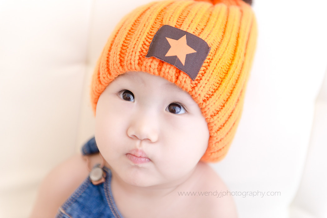 One year old girl wearing an orange beanie hat.