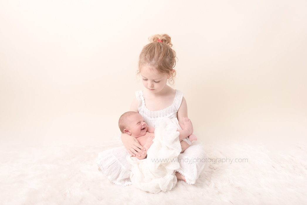 Newborn baby boy held by his big sister. Fine art baby and family photography by Wendy J Photography.