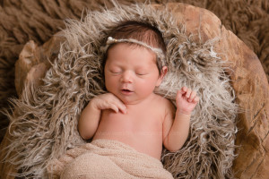 Newborn baby girl lying in a natural wooden bowl.