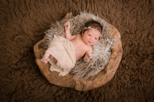 Newborn baby girl lying in a natural wooden bowl.