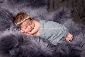 Sleeping newborn baby girl lying on grey sheepskin fur.