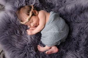 Sleeping newborn baby girl lying on grey sheepskin fur.